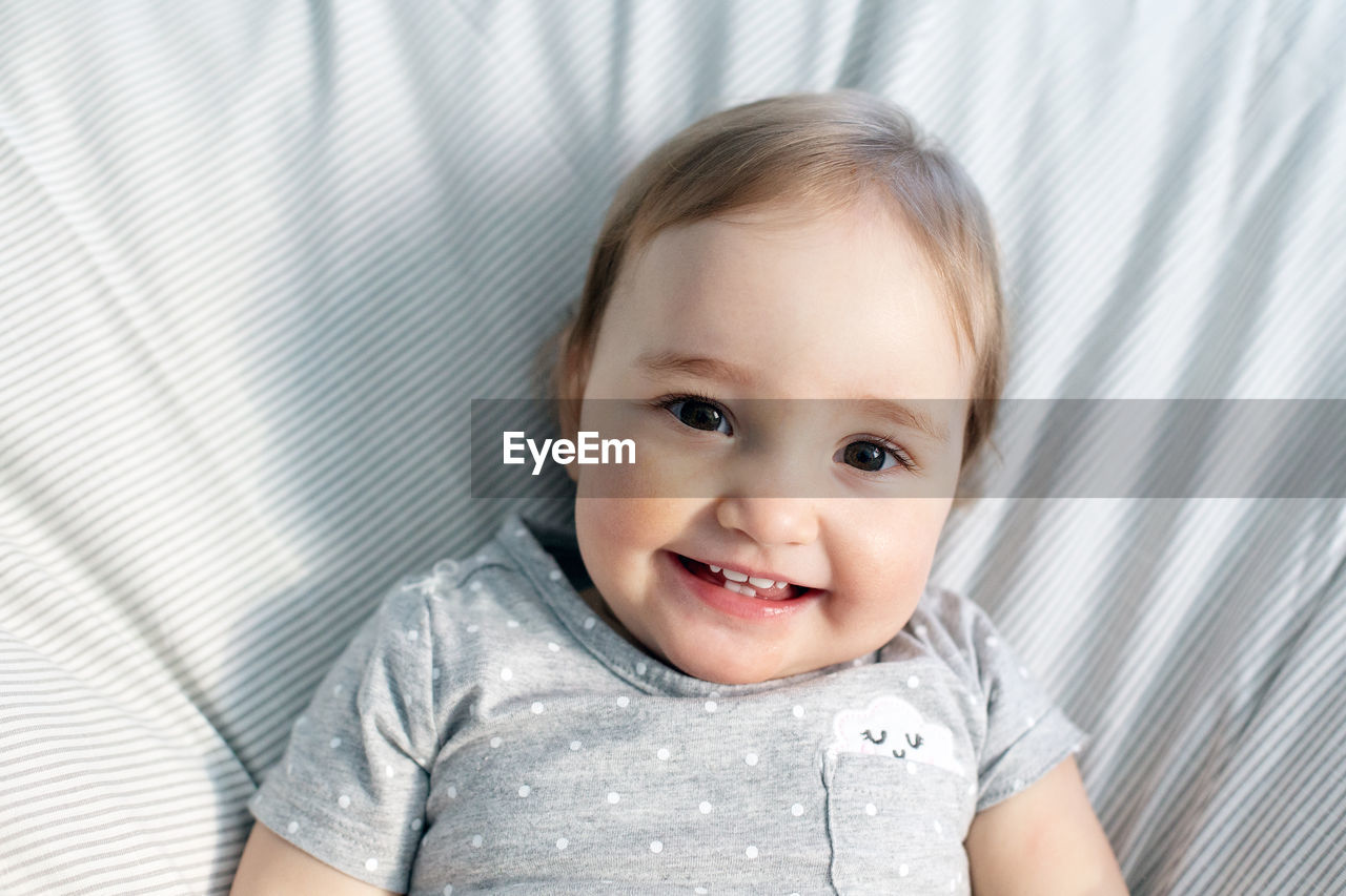 Cute smiling baby girl laying in the bed in morning sun light. grey colors