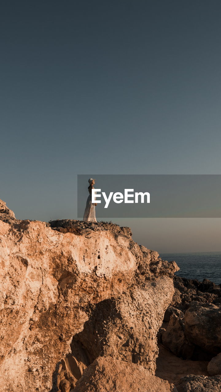 Distant view of woman standing by cliff against sky