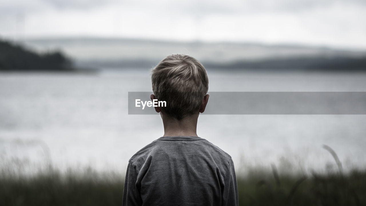 Rear view of boy standing on field against sea