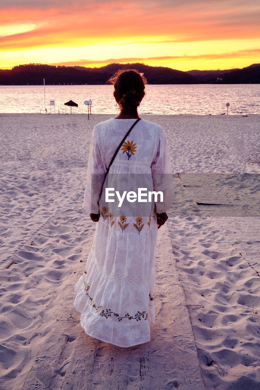 Portrait of young woman standing at beach during sunset