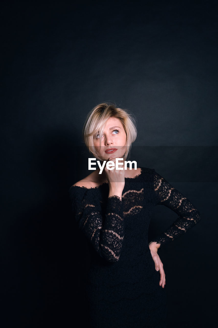 Thoughtful woman in dress standing against black background