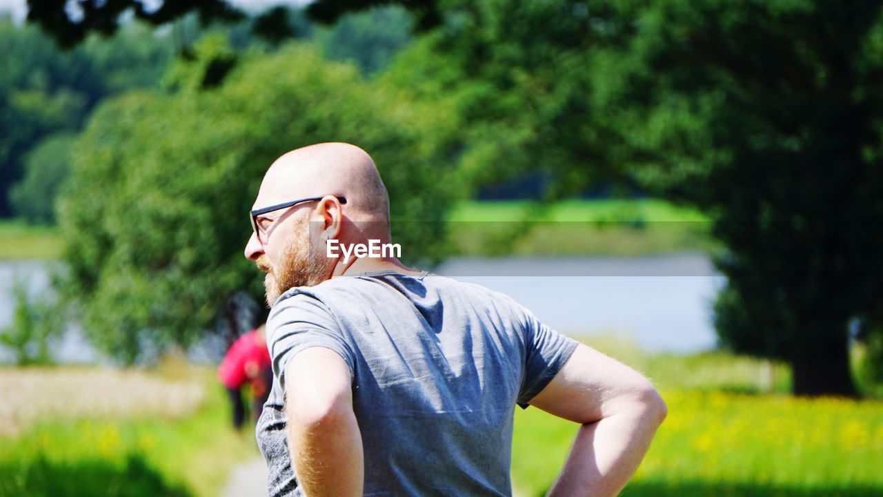 Rear view of bald man on field during sunny day