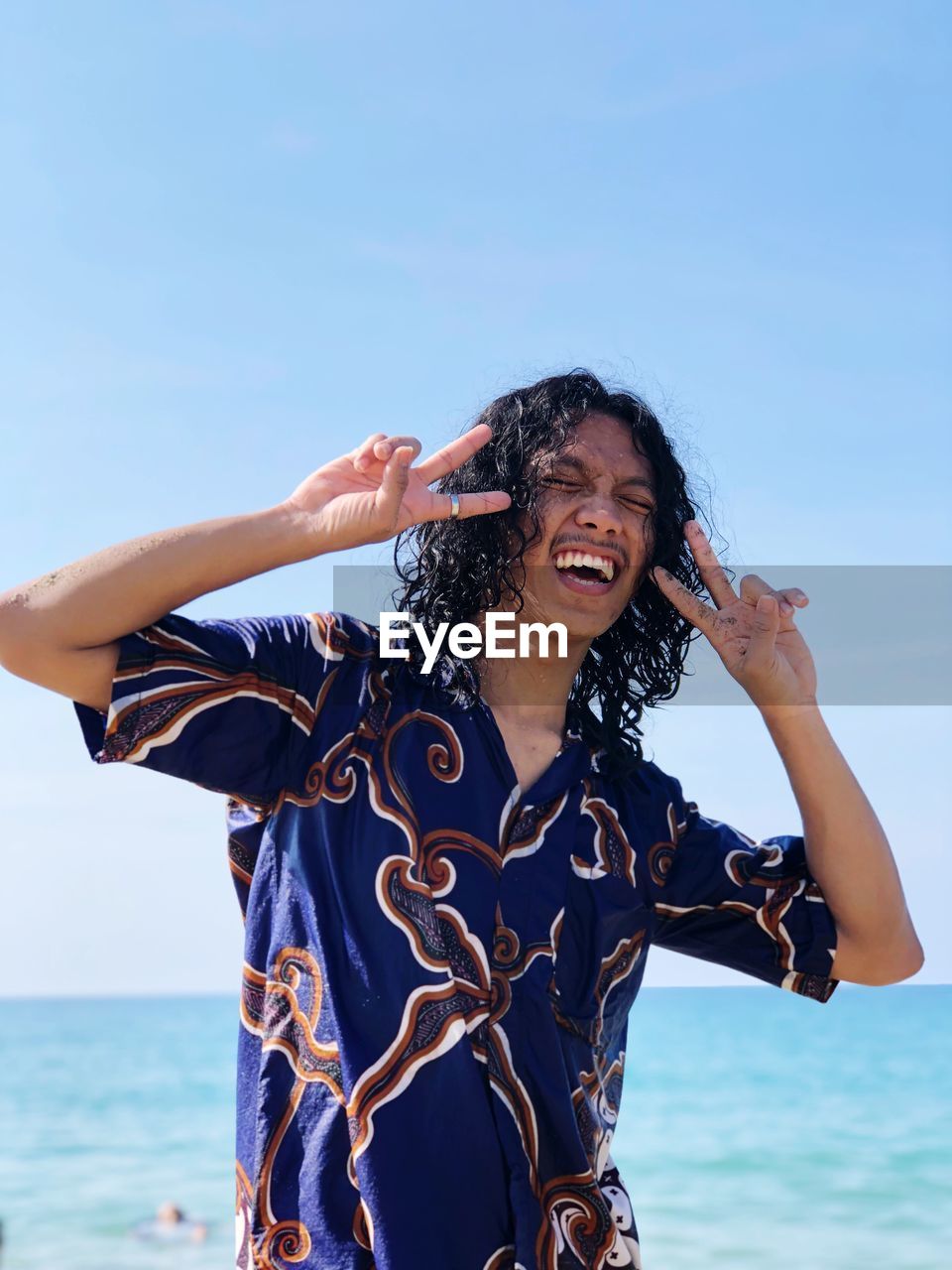 Smiling man gesturing while standing against sea and clear sky