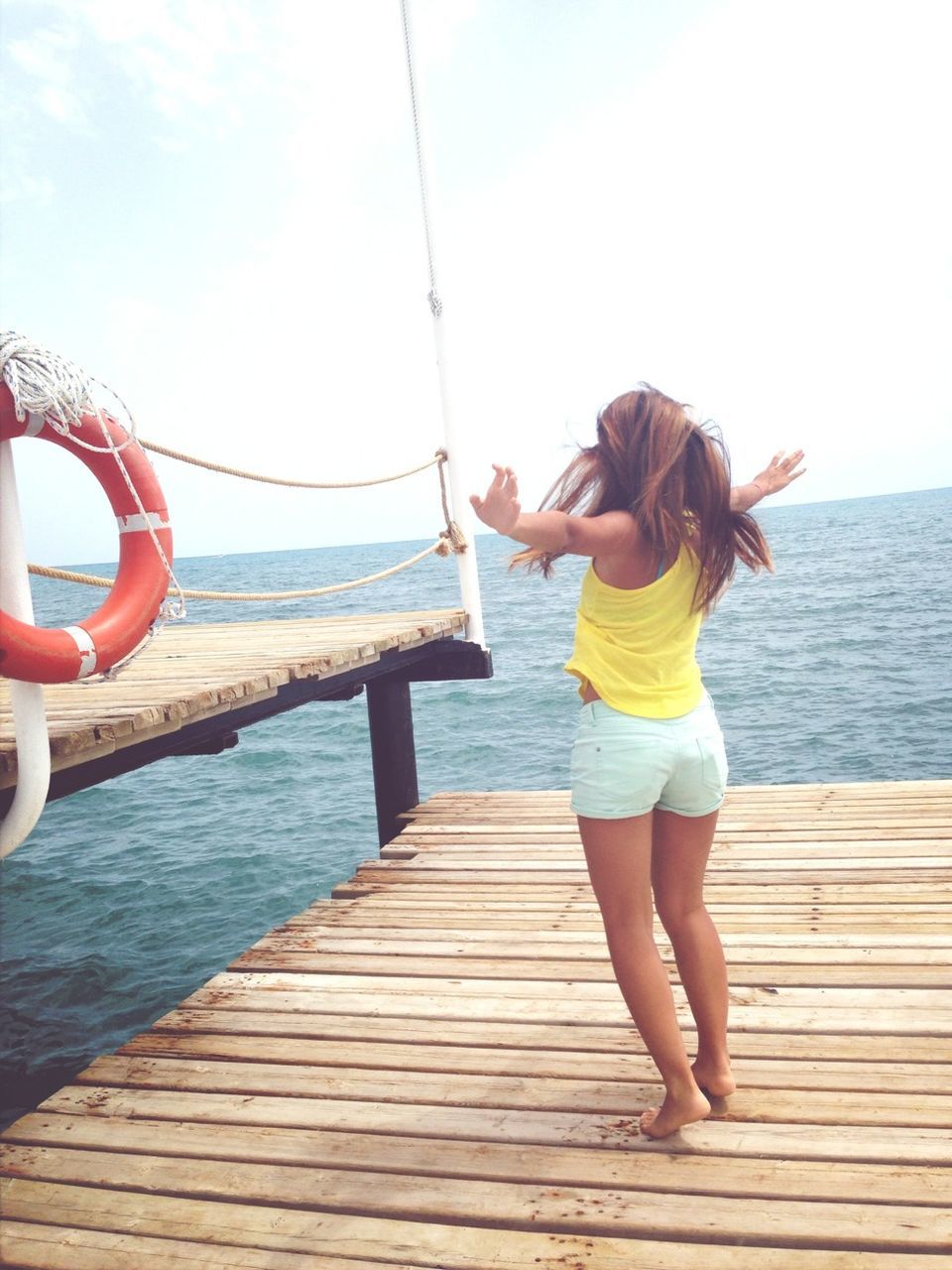 A young woman stands alone on a dock while stretching