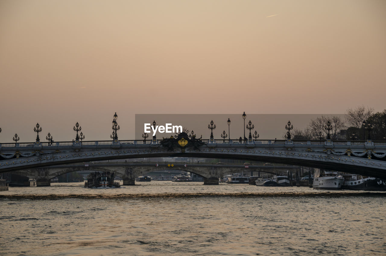 BRIDGE OVER RIVER AGAINST SKY DURING SUNSET