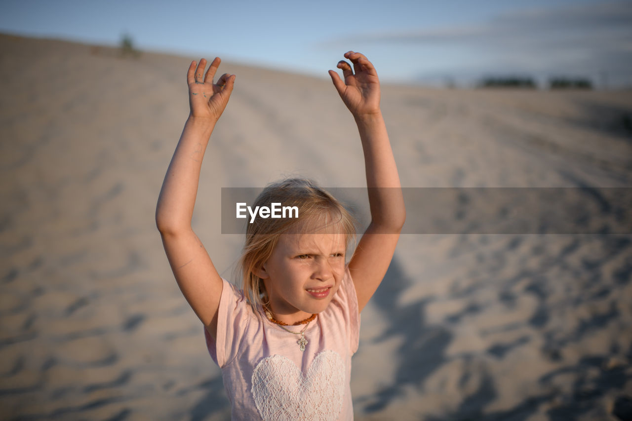 Rear view of girl with arms raised standing at beach