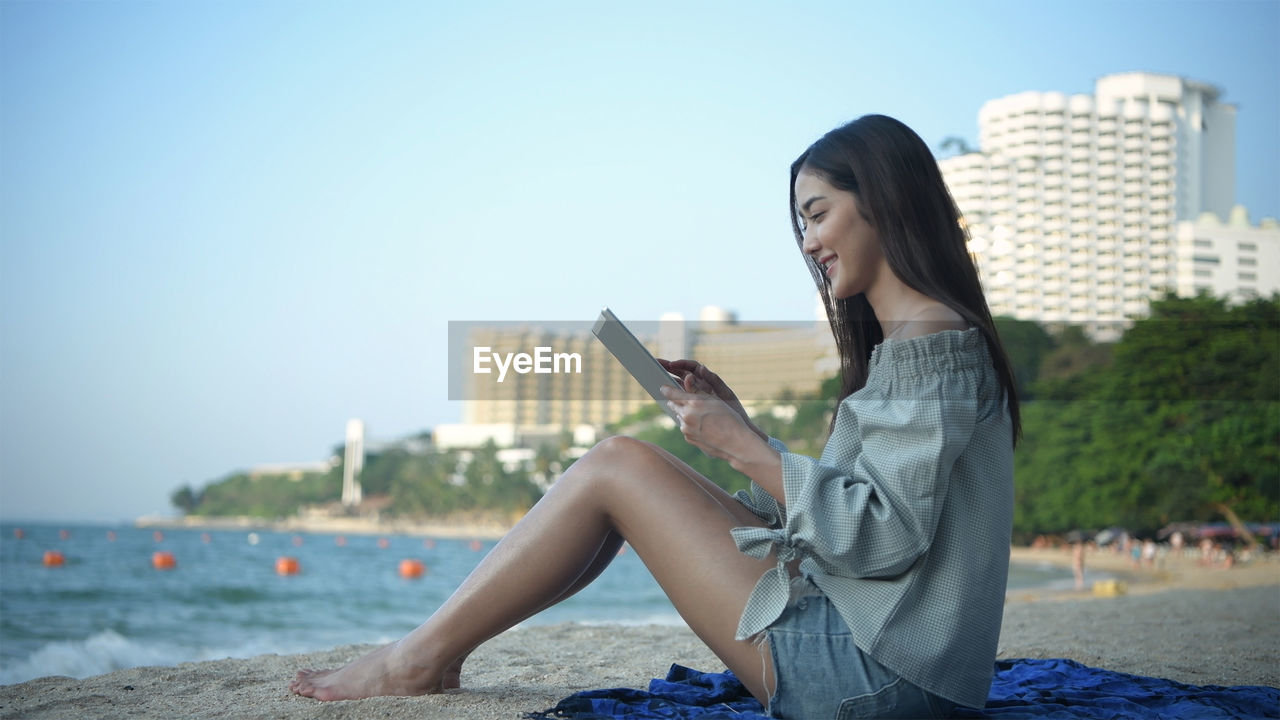 YOUNG WOMAN USING SMART PHONE AGAINST SKY