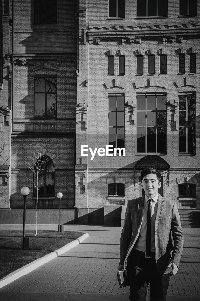 Portrait of man standing on footpath against building