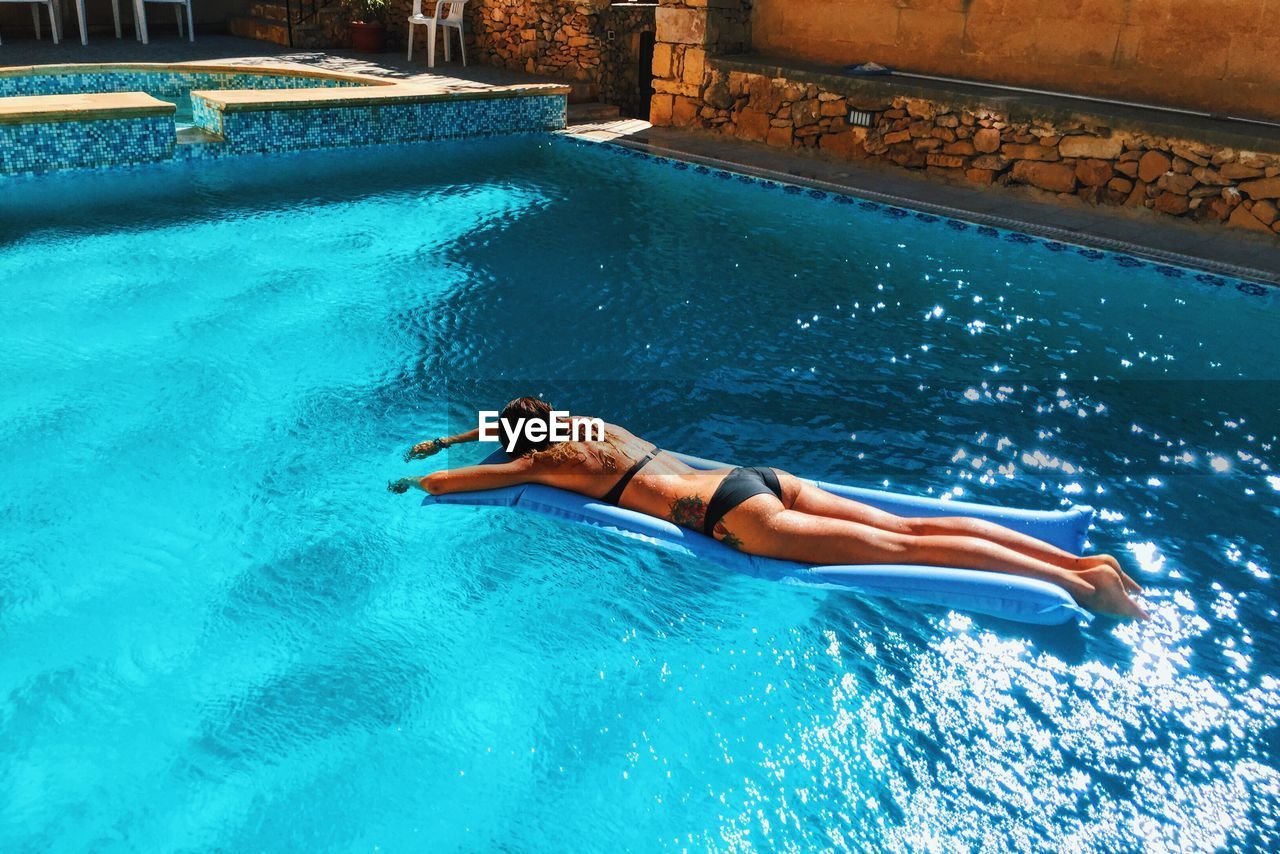 High angle view of sensuous woman in bikini relaxing on raft at swimming pool