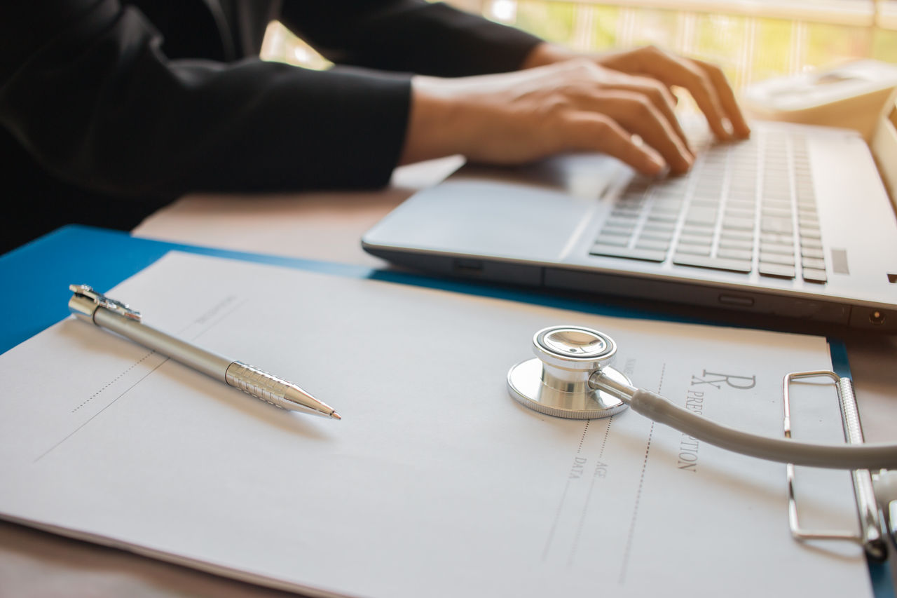 Cropped image of doctor using laptop at desk in office