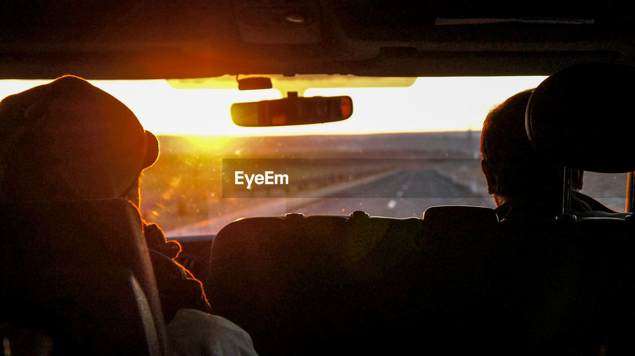 Rear view of men sitting in car during sunset