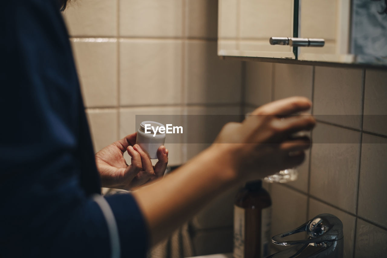 Cropped image of woman holding glass and pills while standing in bathroom