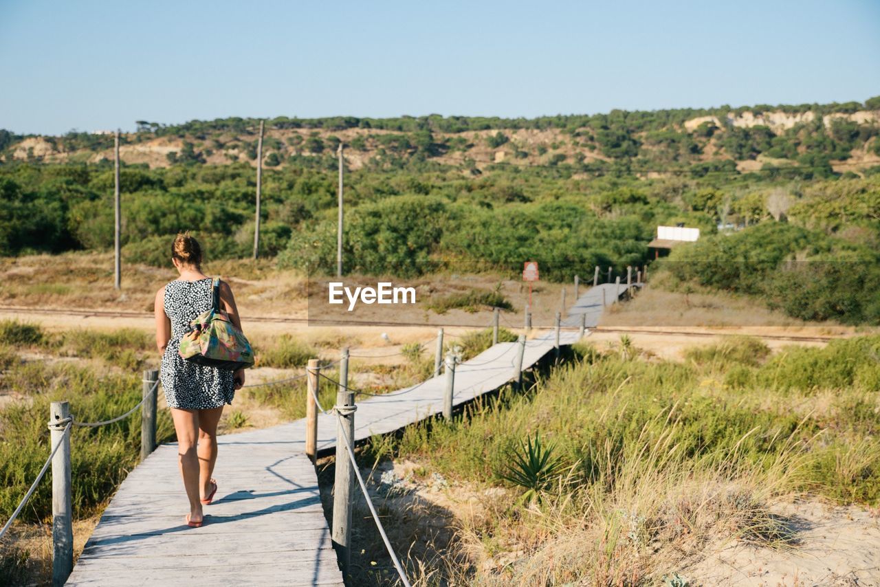 REAR VIEW OF WOMAN WALKING ON ROAD AGAINST SKY