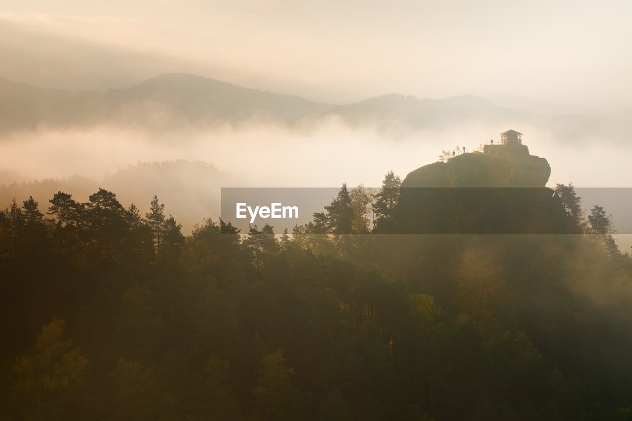 Misty daybreak in a valley of bohemian switzerland park. hill with hut on hill in magical darkness.