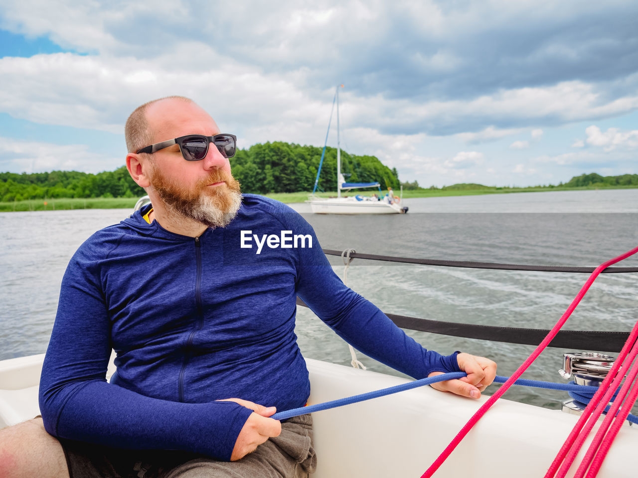 Adult bearded man using a winch to pull a blue rope on a sailboat or sailing yacht