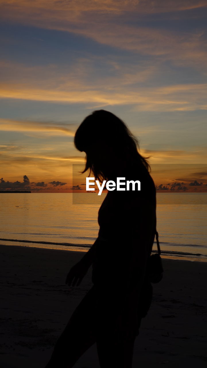 Silhouette woman standing on beach against sky during sunset