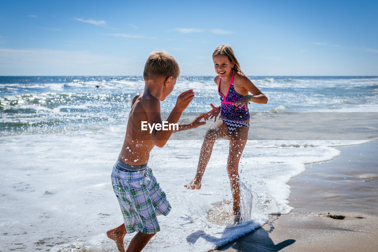 Siblings playing at beach against sky