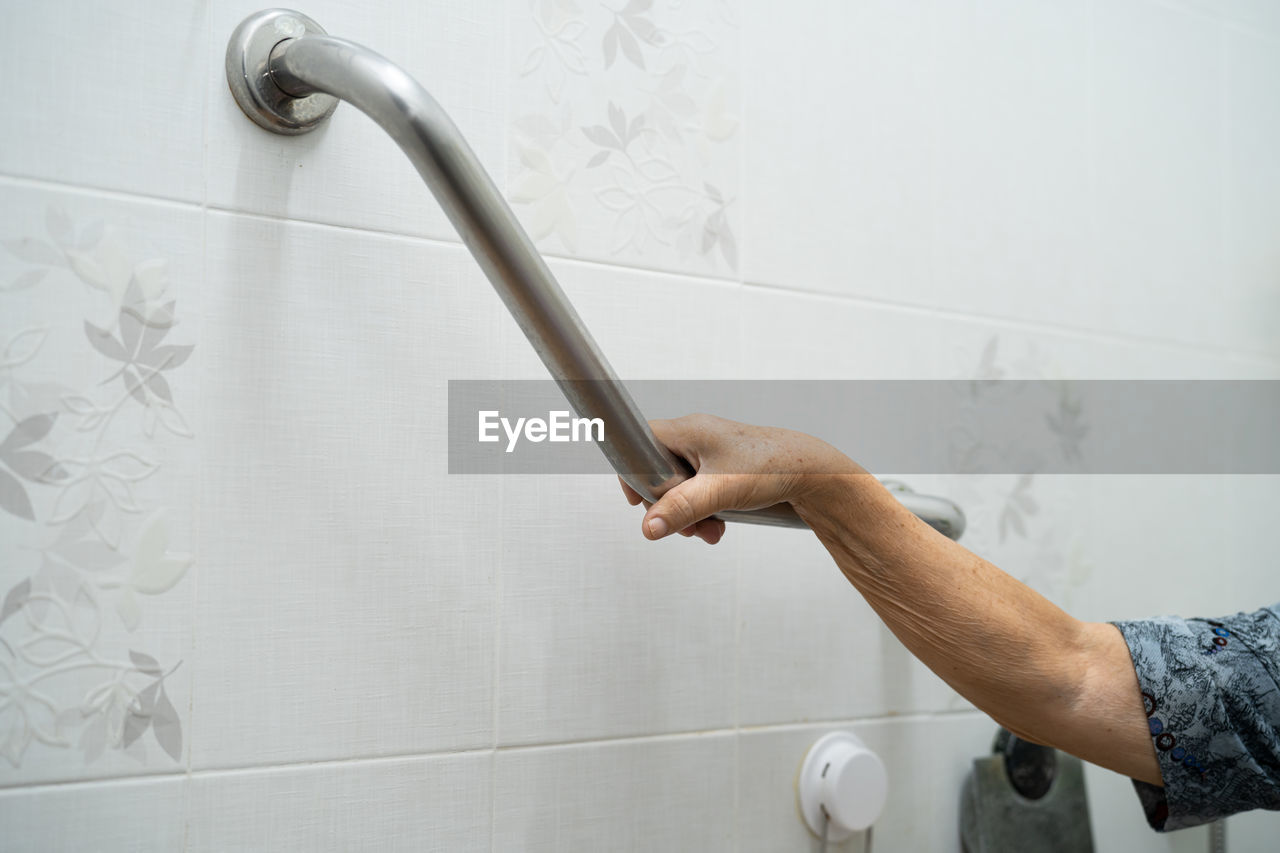 Midsection of man holding faucet against wall