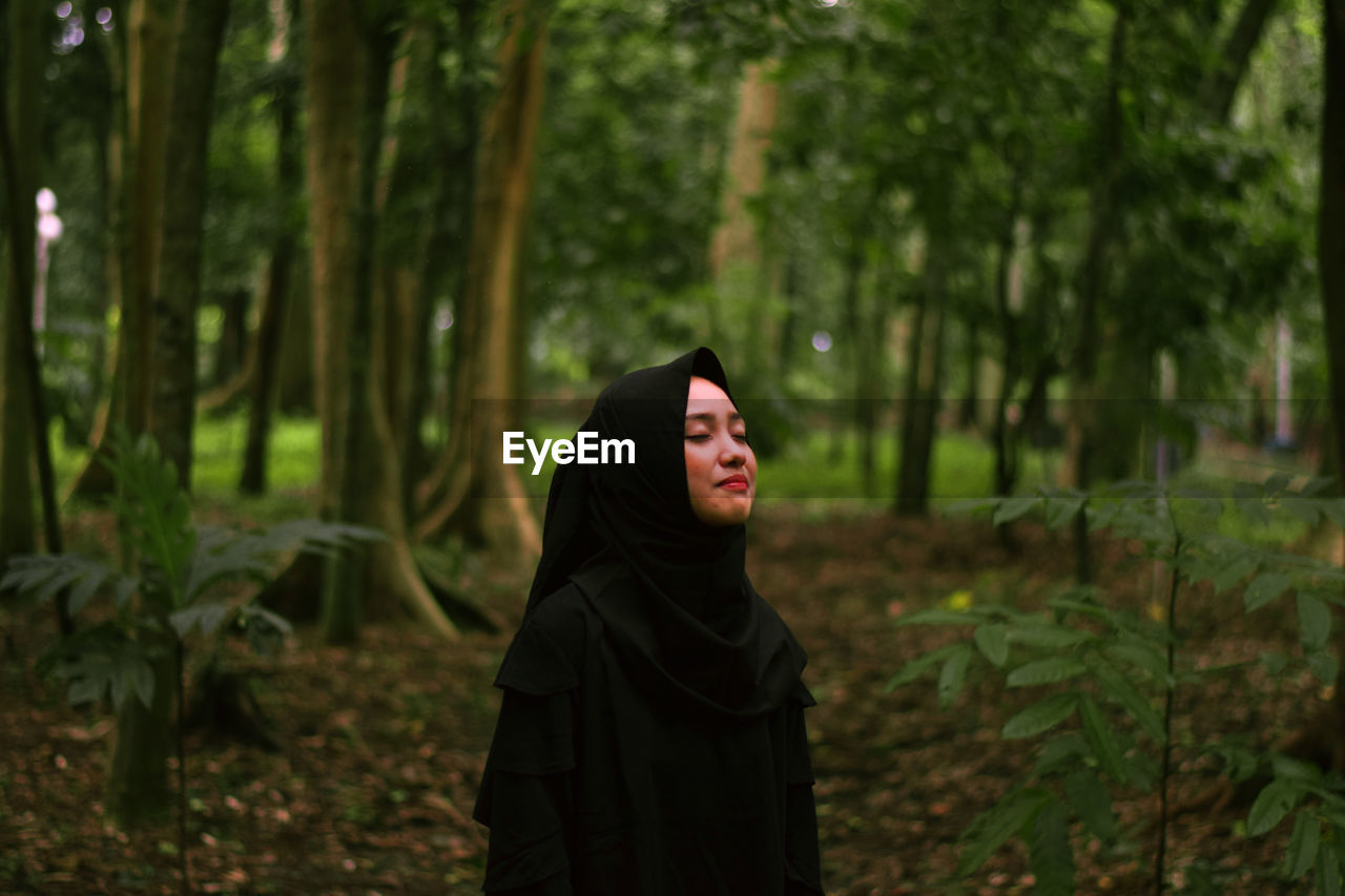 Woman with eyes closed standing against trees in forest