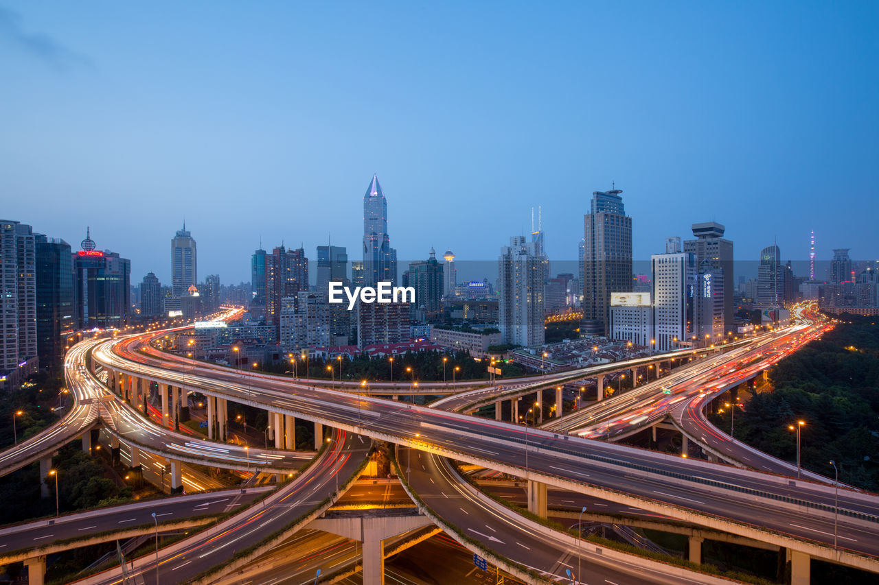 High angle view of light trails on road amidst buildings in city against sky