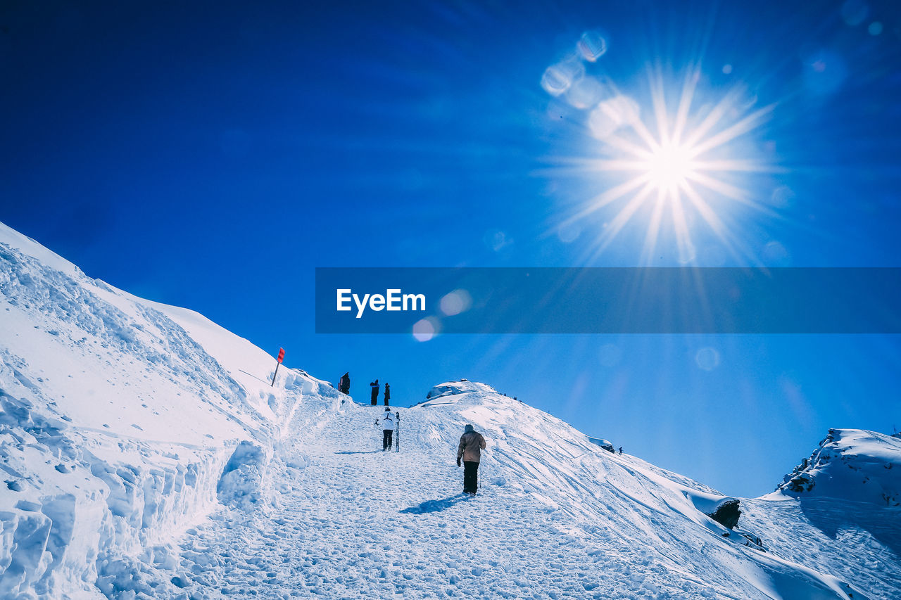 People skiing on snowcapped mountain against blue sky