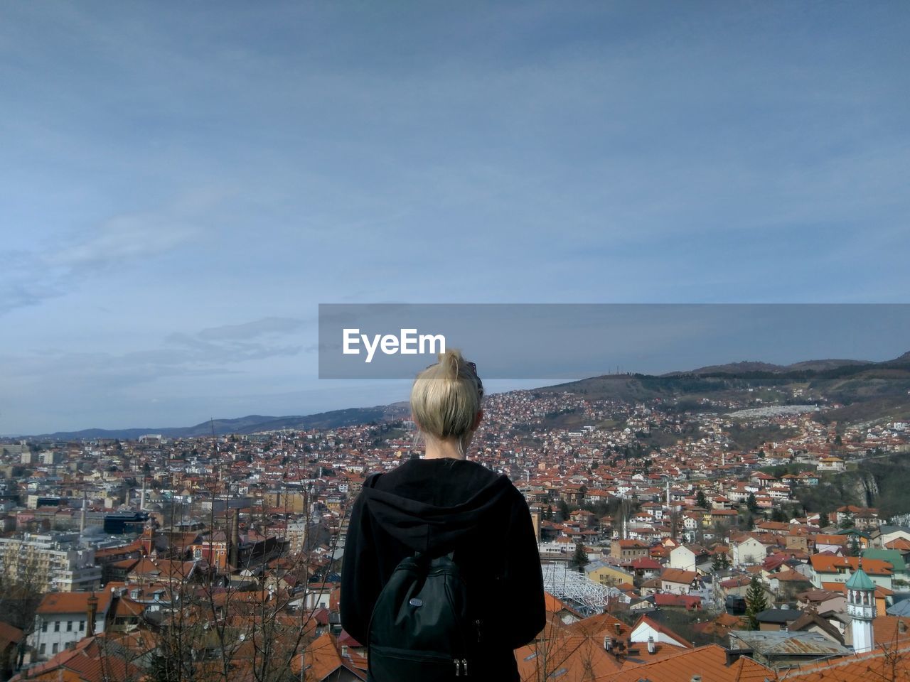 Rear view of woman looking at cityscape against blue sky