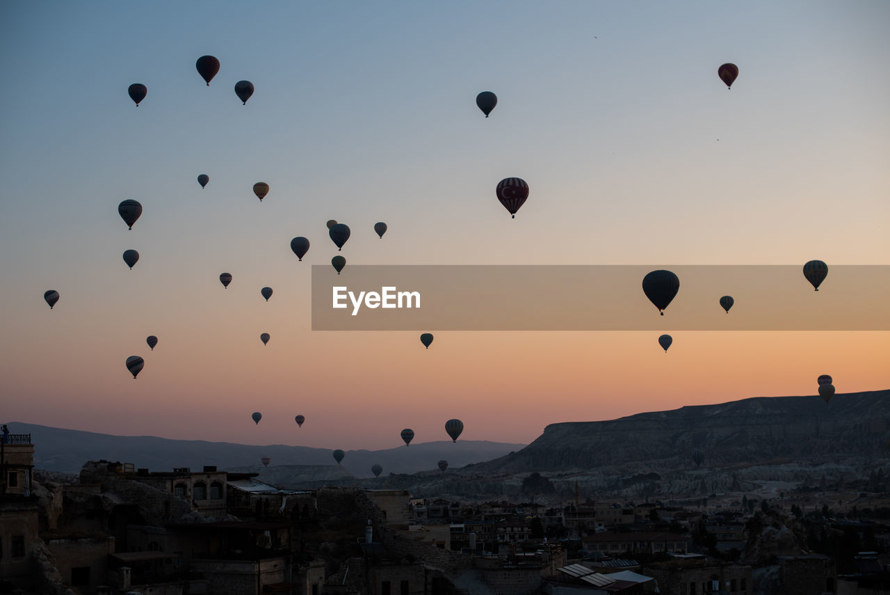 Hot air balloons flying over city against sky during sunset