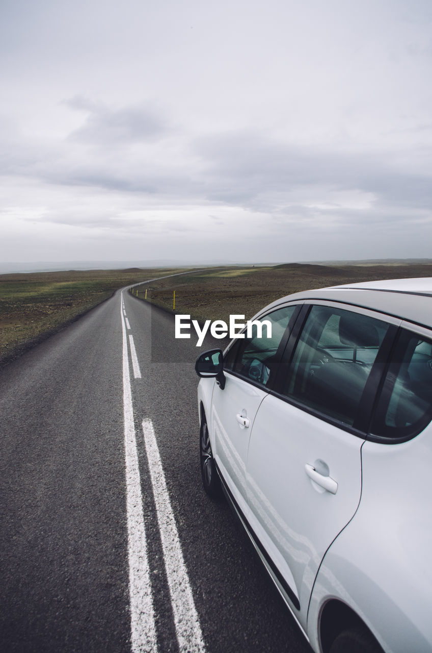 Car on road amidst landscape against cloudy sky