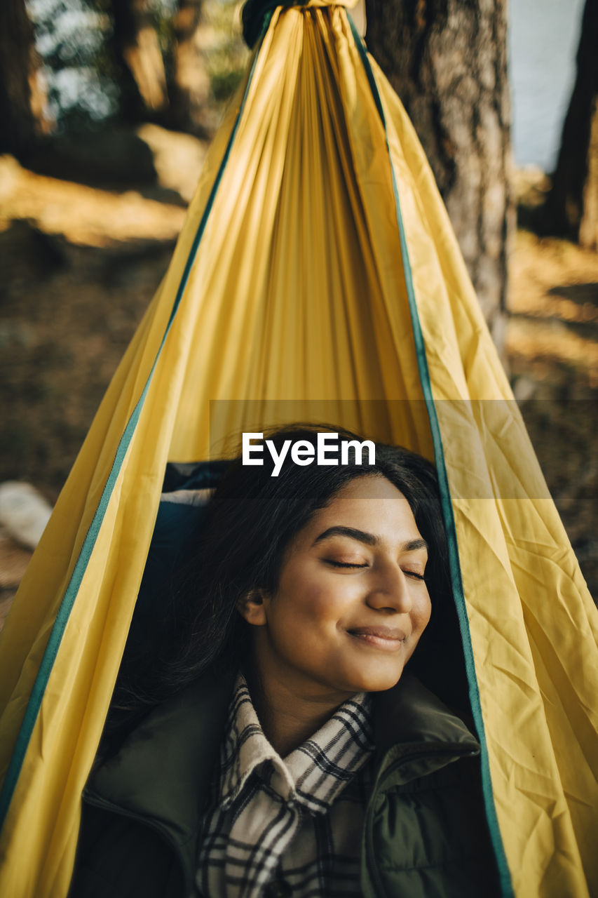 Smiling woman with closed eyes on hammock in forest during vacation