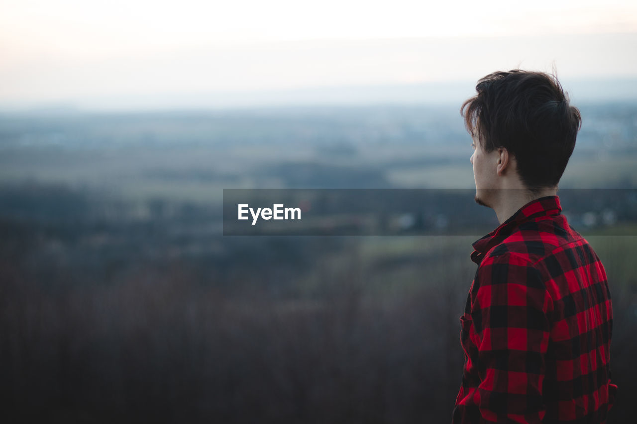 Candid portrait of a man in his 20s dressed in a black and red checked shirt looking into his future