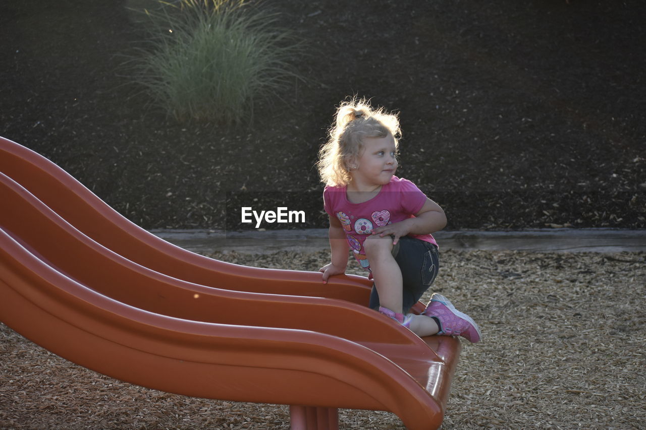 Cute girl kneeling on slide in playground