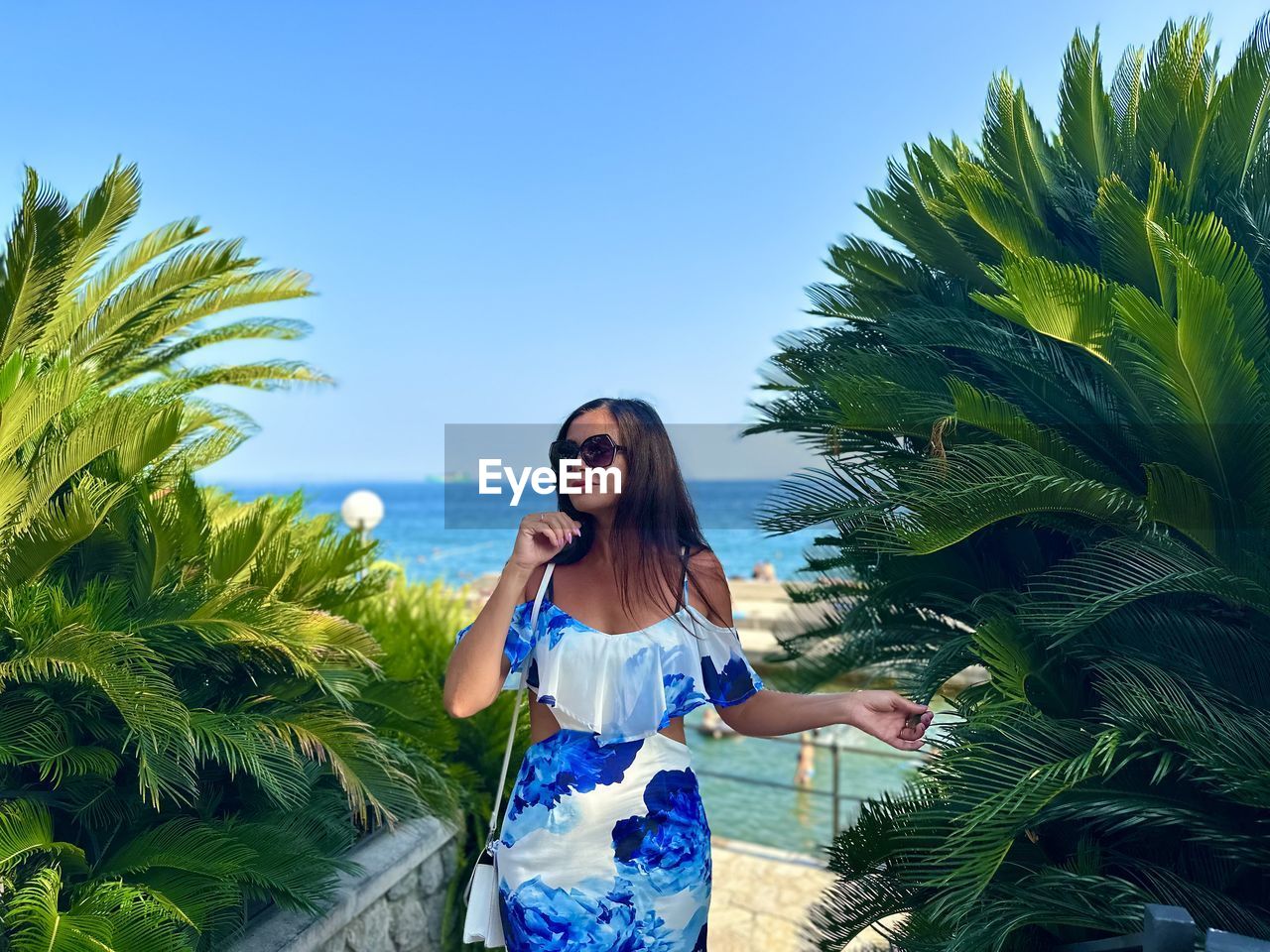 young woman standing against palm tree against clear sky