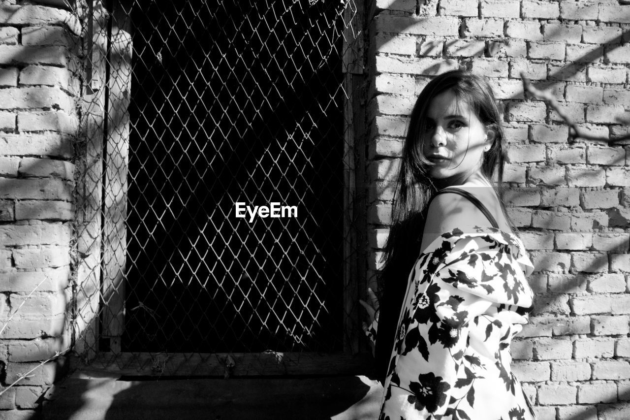 Portrait of confident woman standing against brick wall