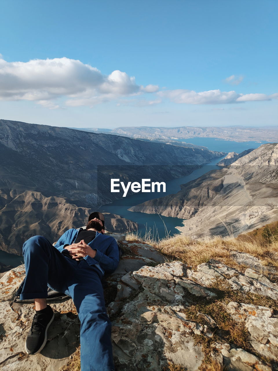 MAN SITTING ON ROCKS AGAINST SKY