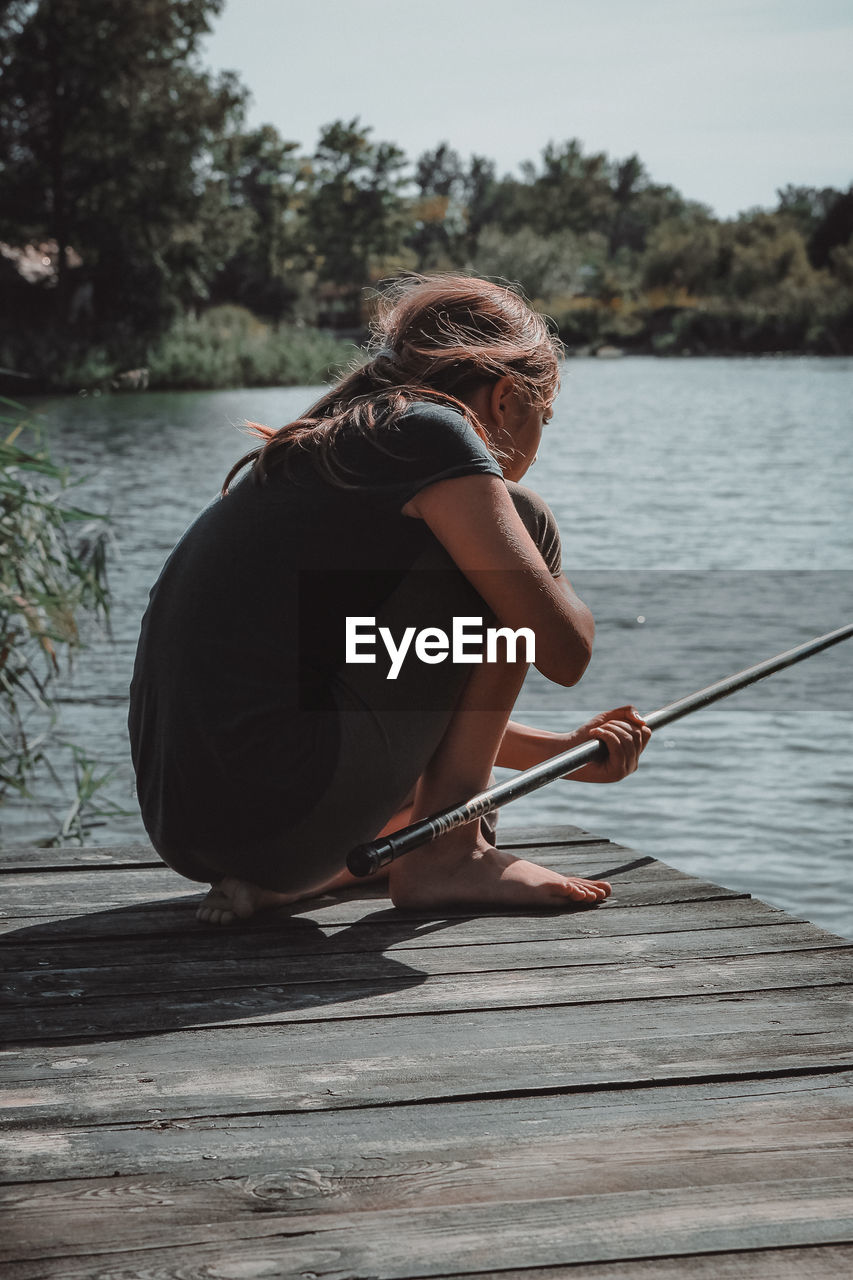 Girl fishing while crouching on pier