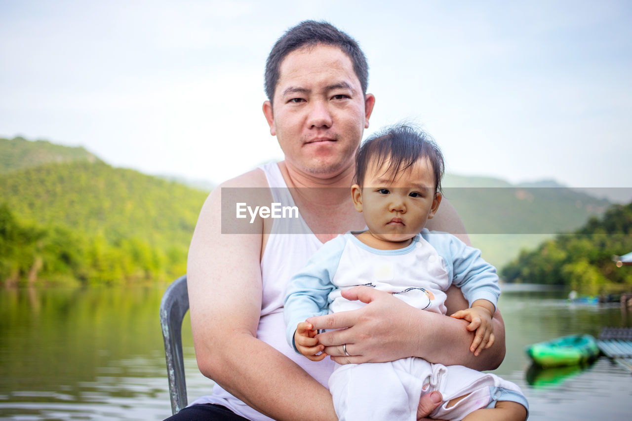 Portrait of father and daughter sitting against lake