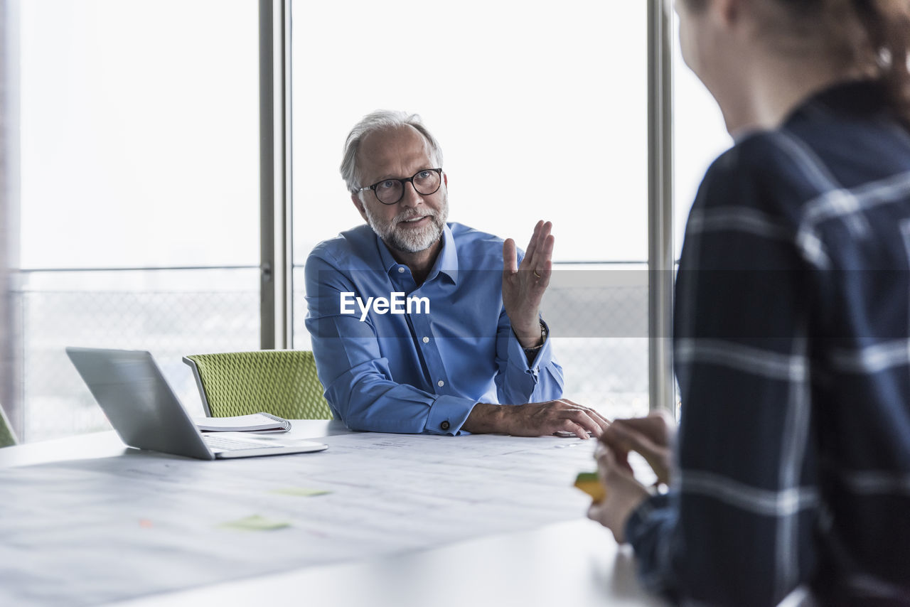 Mature businessman and young woman talking in conference room in office