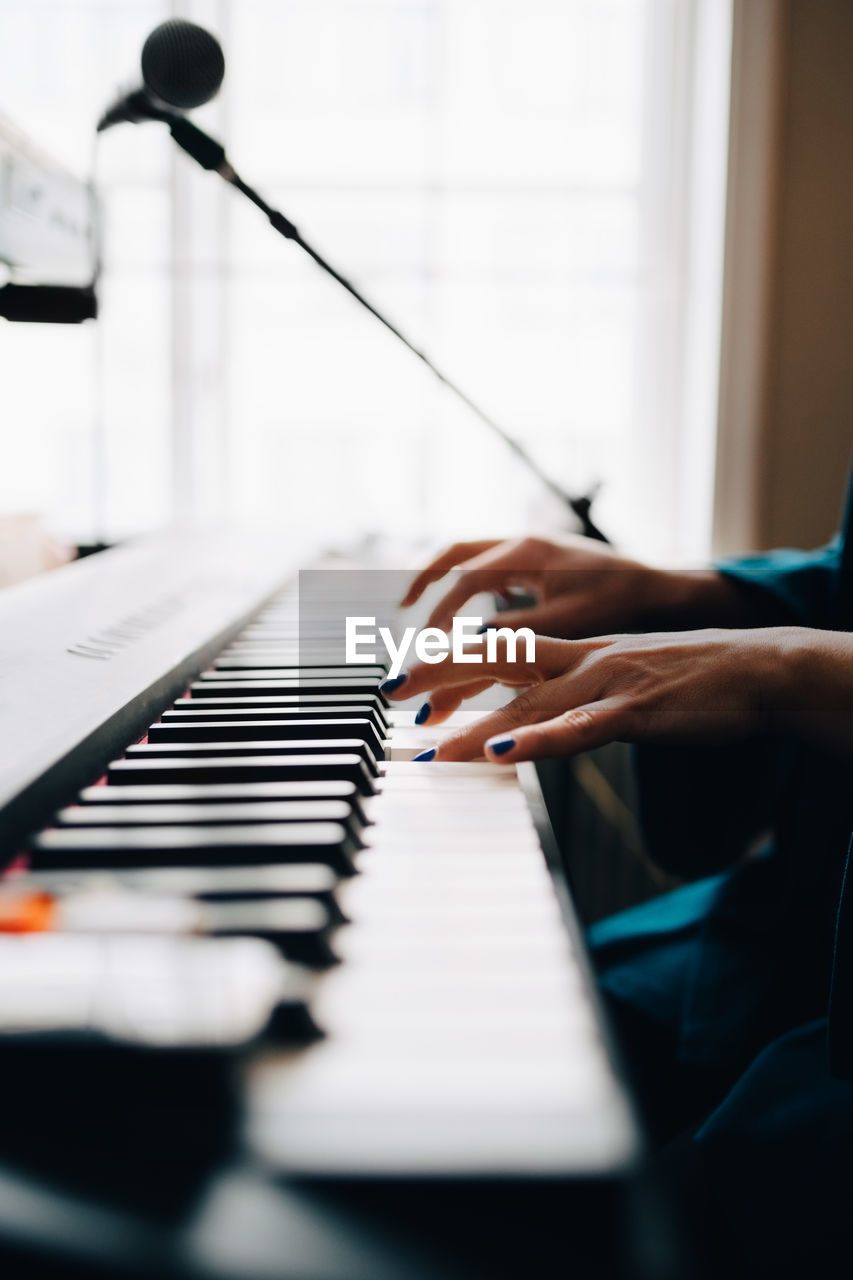 Cropped image of woman playing piano by window at studio