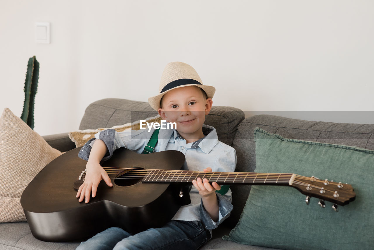 Boy smiling whilst playing guitar with a hat on at home