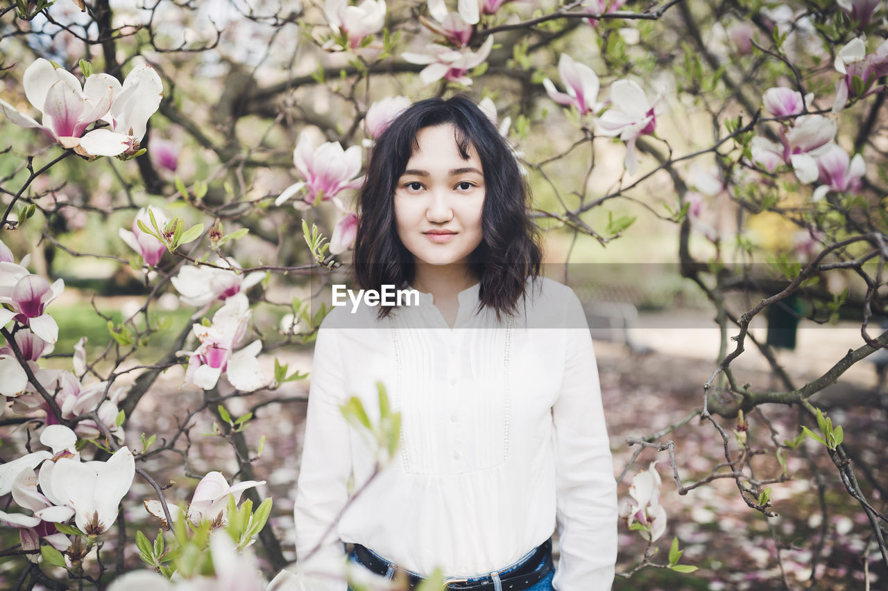 Happy asian young woman under the blooming magnolia tree, smiling