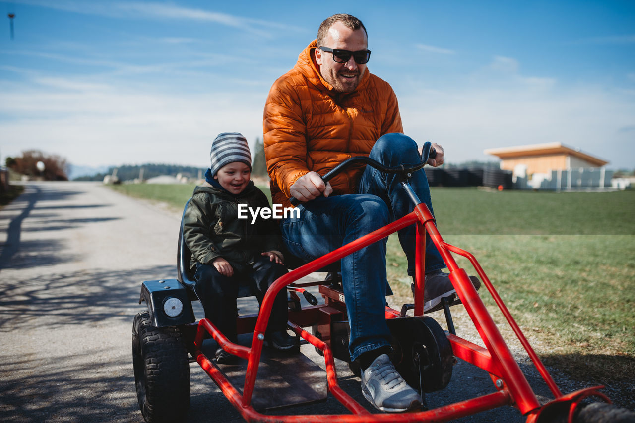 Father and son smiling having fun riding a cart in a park in winter