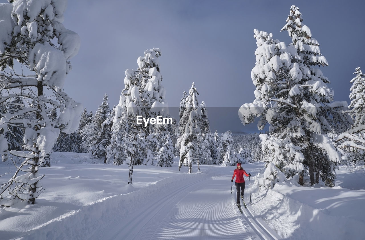 Senior woman skiing over snow path in forest