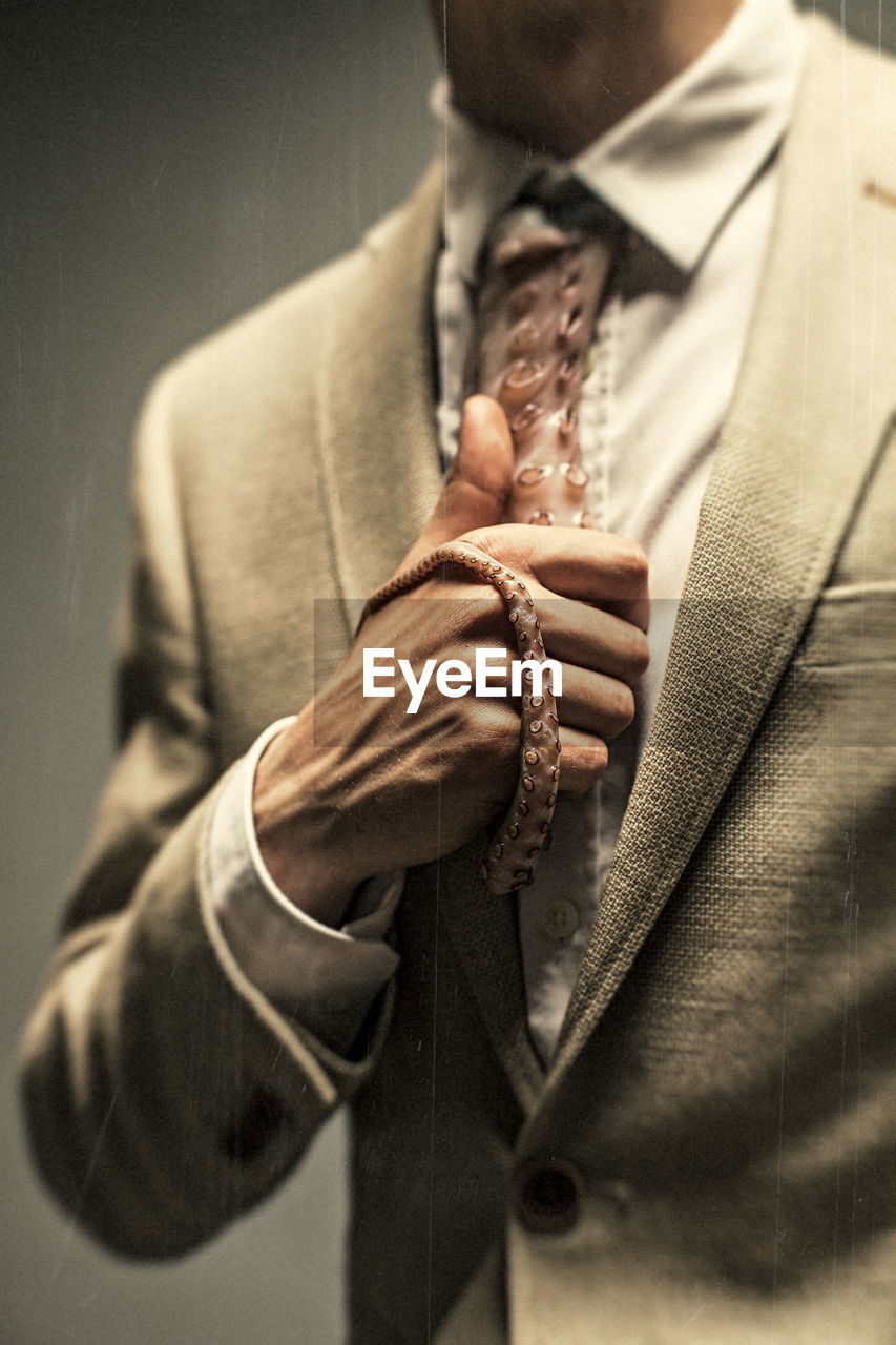 Midsection of businessman holding tentacle necktie while standing against gray background