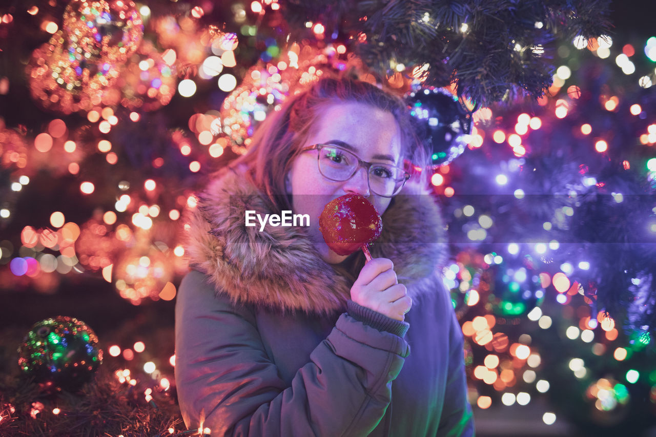Portrait of young woman eating caramelized apple during christmas at night