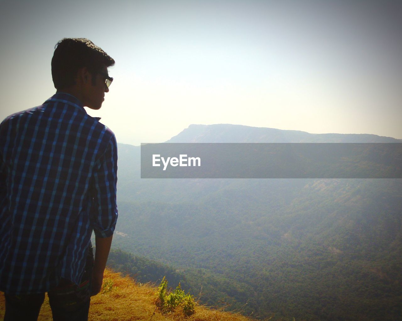 YOUNG MAN LOOKING AT MOUNTAIN RANGE AGAINST SKY