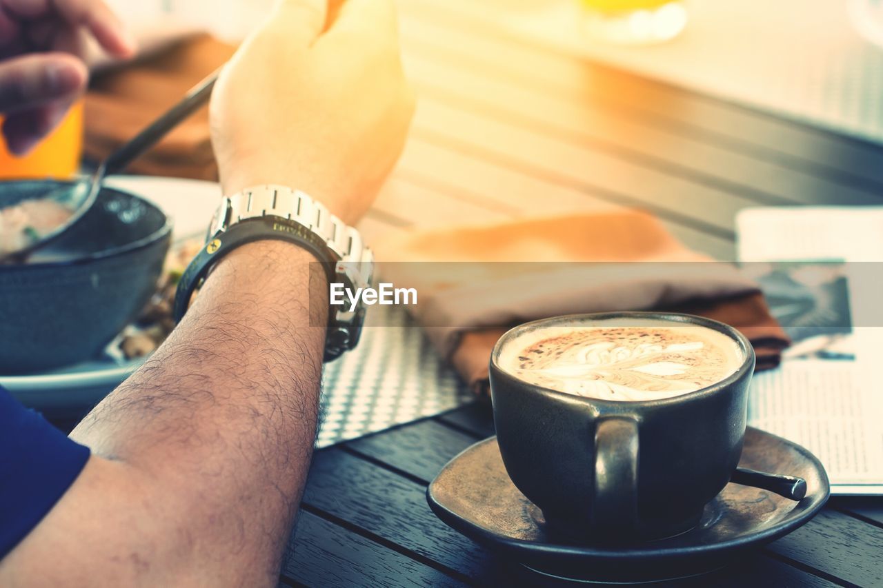 CLOSE-UP OF HAND HOLDING COFFEE CUP WITH CAFE