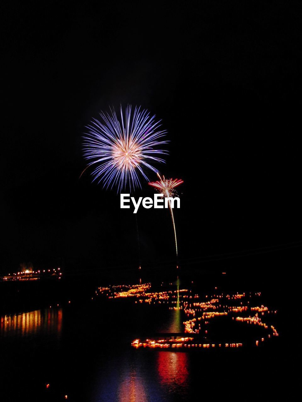 LOW ANGLE VIEW OF FIREWORK DISPLAY OVER RIVER AGAINST SKY AT NIGHT