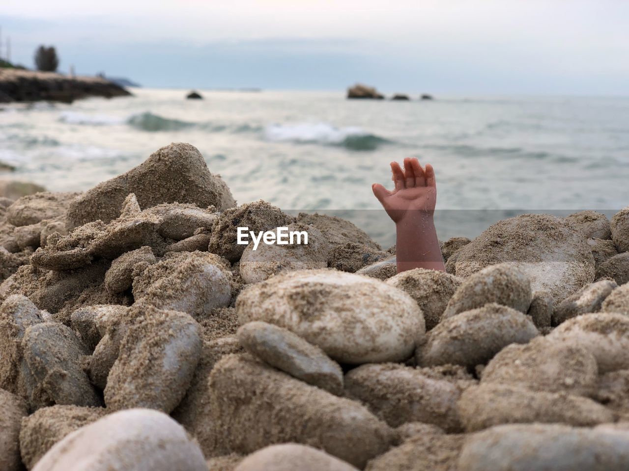 Person hand amidst pebbles at beach against sky