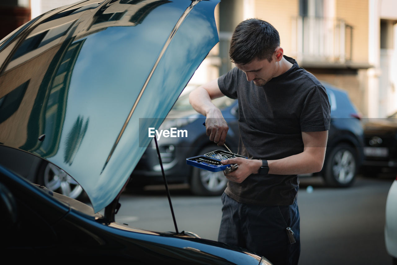 A young man takes a screwdriver out of a car repair box.