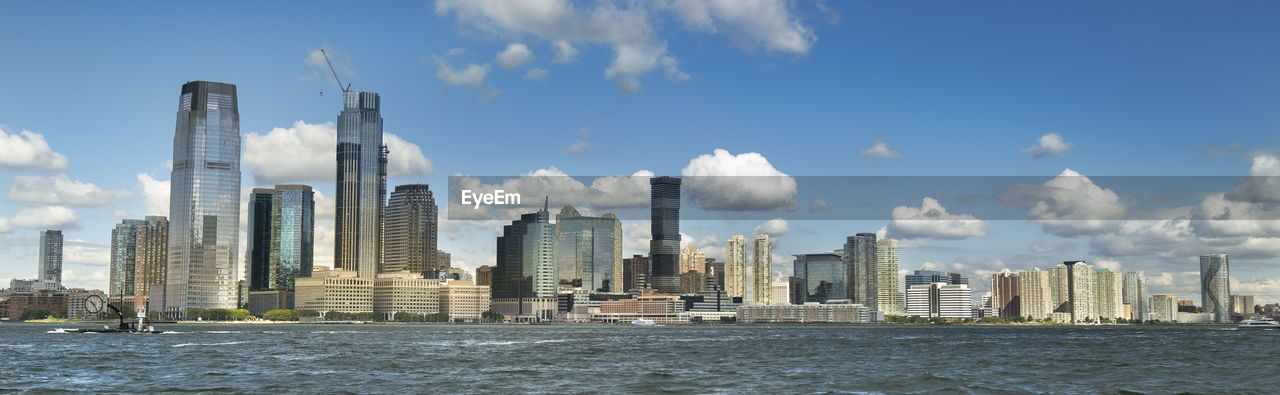 SEA BY MODERN BUILDINGS AGAINST SKY IN CITY SKYLINE